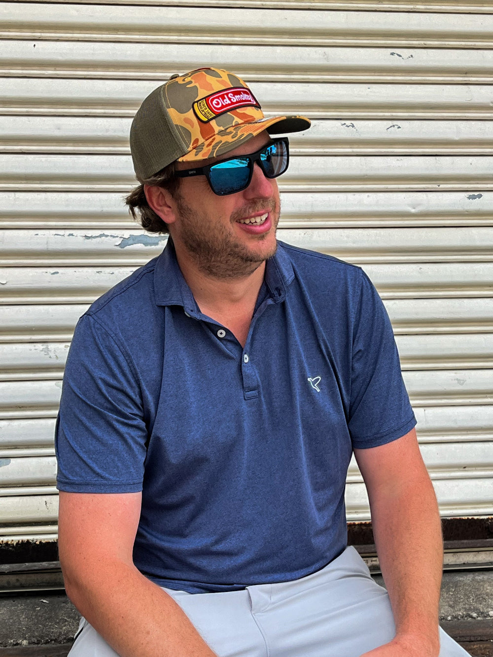 Man wearing a camo Old Smokey logo hat with the logo in the style of a red shotgun shell