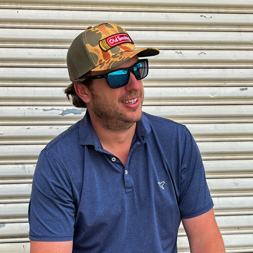 Man wearing a camo Old Smokey logo hat with the logo in the style of a red shotgun shell