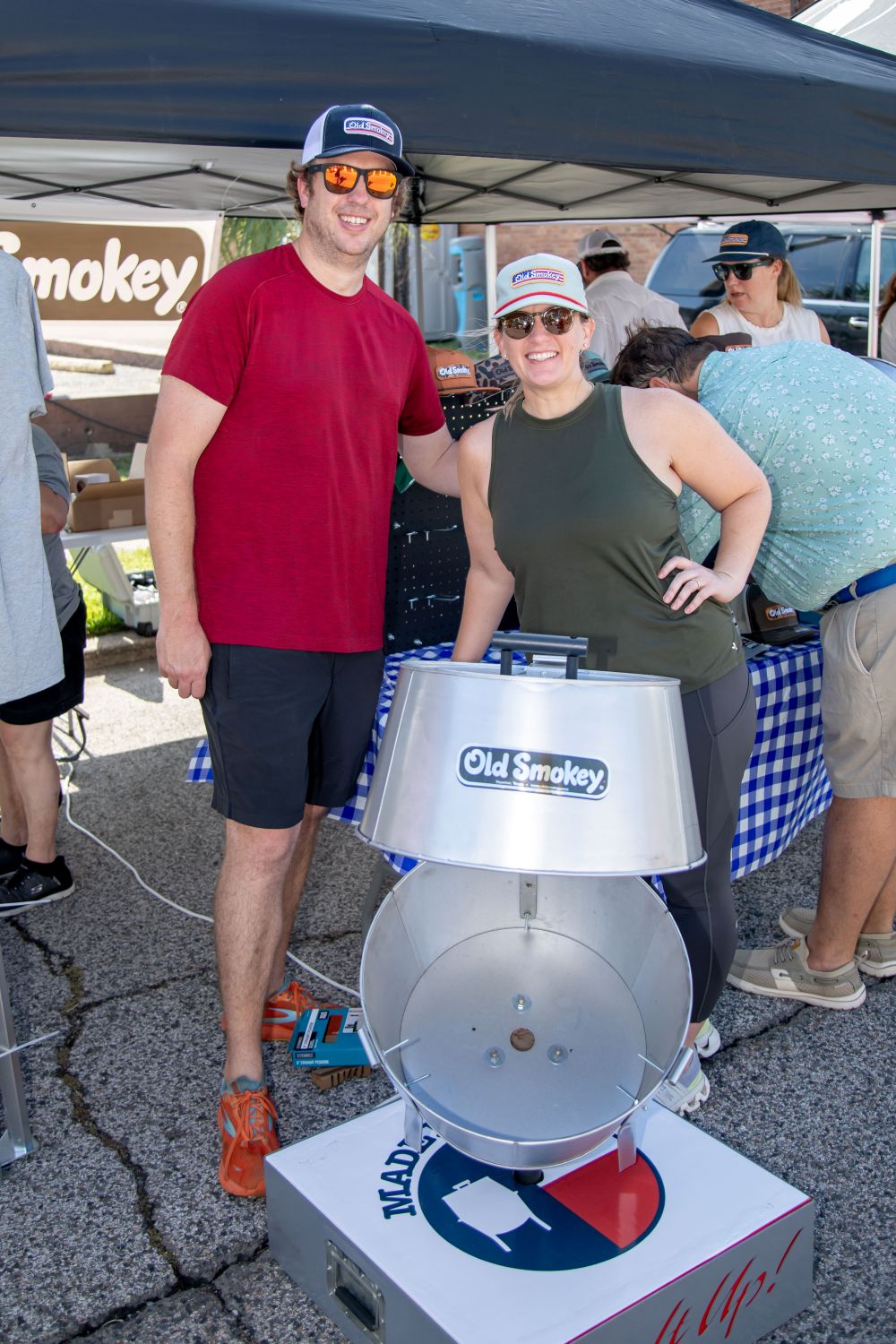 Two people posing behind an open Old Smokey Charcoal Grill at an Old Smokey Throwdown event