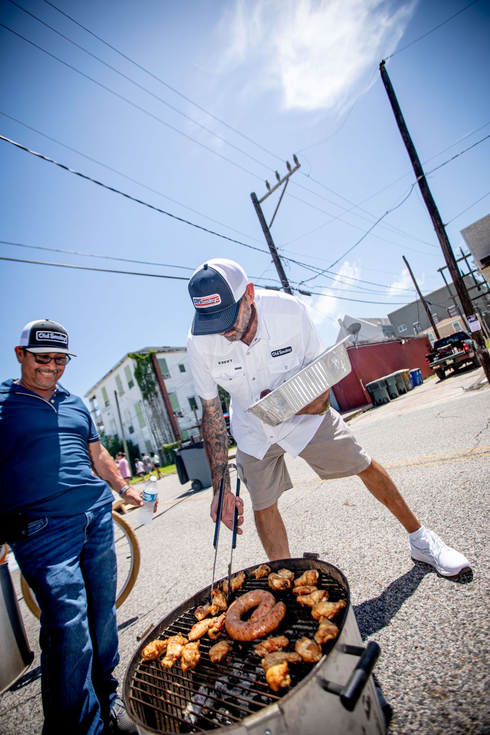 Two men grilling food on a street with a clear blue sky.