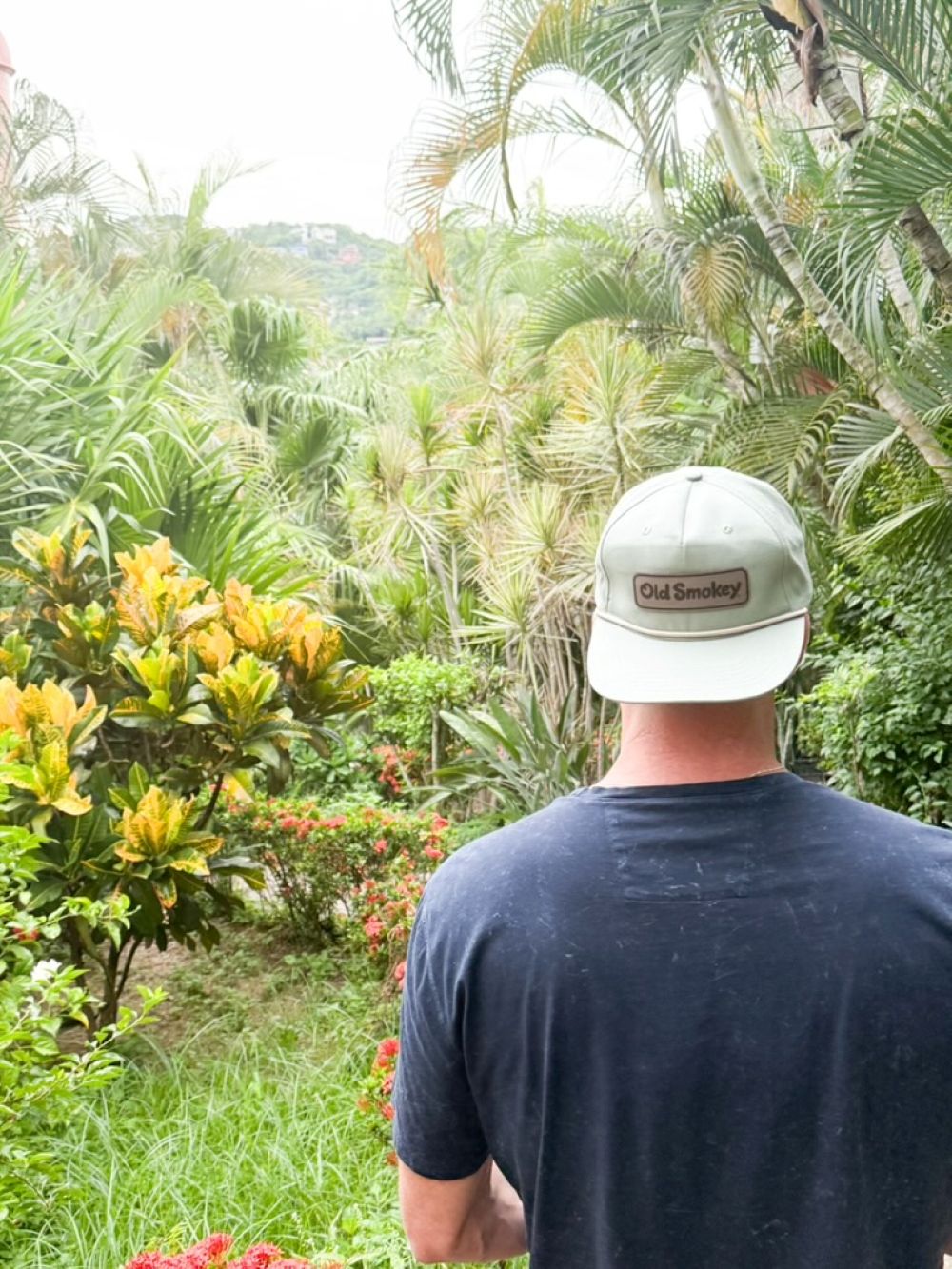 Person wearing an Old Smokey hat and dark shirt standing in a lush, green Hawaiian setting
